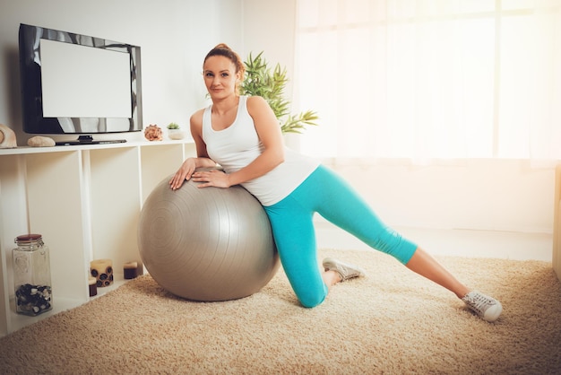 Mooie gespierde lachende jonge vrouw die thuis rust na training met pilates bal. Camera kijken.