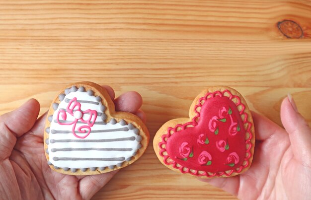 Mooie gevormde hartvormige koekjes in de handen van het paar samengesteld op houten achtergrond