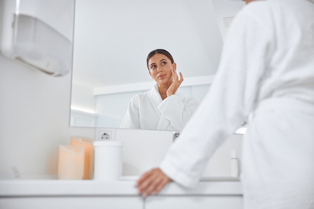 Mooie gezonde glimlachende blanke vrouw die voor haar huid in de badkamer zorgt