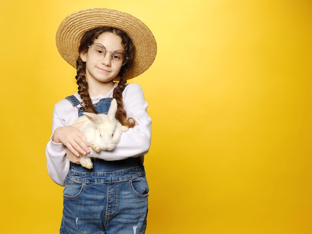 Mooie glimlach schoolmeisje met een schattig echt konijntje isoleerde gele achtergrond