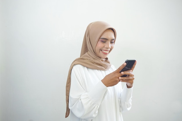 Mooie glimlachende Aziatische Moslimvrouw die hijab draagt die mobiele telefoon gebruikt die op witte achtergrond wordt geïsoleerd