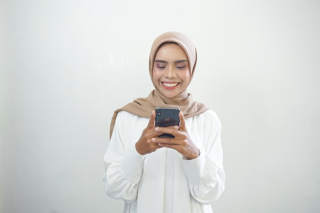 Mooie glimlachende Aziatische Moslimvrouw die hijab draagt die mobiele telefoon gebruikt die op witte achtergrond wordt geïsoleerd