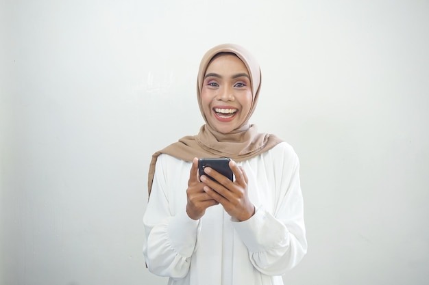 Mooie glimlachende Aziatische Moslimvrouw die hijab draagt die mobiele telefoon gebruikt die op witte achtergrond wordt geïsoleerd