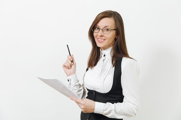 Mooie glimlachende blanke jonge bruinharige zakenvrouw in zwart pak, wit overhemd, bril met papieren werkdocumenten geïsoleerd op een witte muur