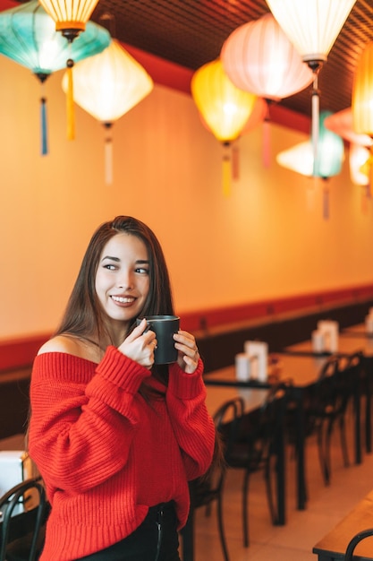 Mooie glimlachende jonge Aziatische vrouw in het rood met kopje thee in het Chinese restaurant