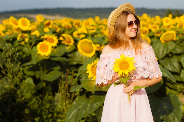 Mooie glimlachende jonge vrouw in een wit overhemd staat in het veld onder de zonnebloemen