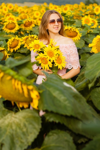 Mooie glimlachende jonge vrouw in een wit overhemd staat in het veld onder de zonnebloemen