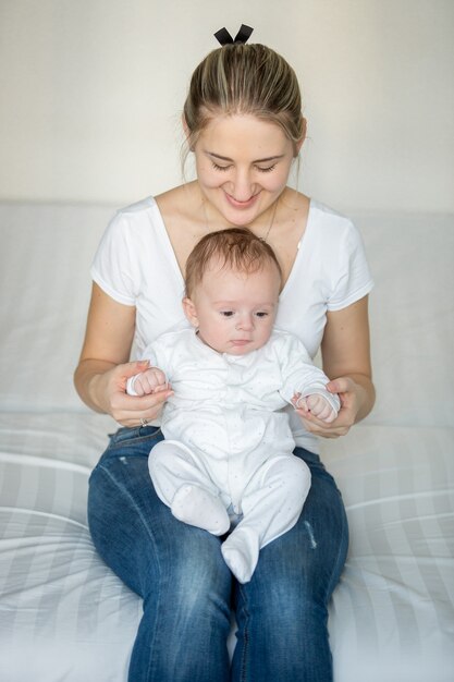 Mooie glimlachende moeder die op bed zit en haar babyjongen vasthoudt