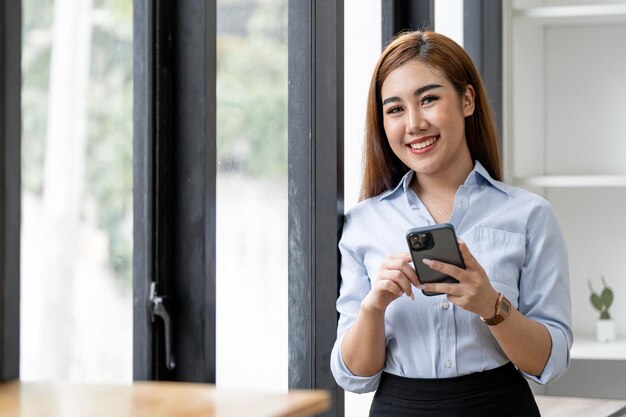 Mooie glimlachende onderneemster die smarphone binnenshuis exemplaarruimte gebruikt