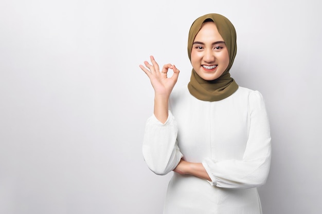 Mooie glimlachende vriendelijke jonge arabische aziatische moslimvrouw die hijab draagt die ok goed teken toont geïsoleerd op witte achtergrond mensen religieuze levensstijl concept