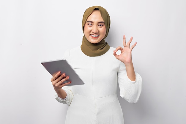 Mooie glimlachende vriendelijke jonge Arabische Aziatische moslimvrouw die hijab groen draagt en digitale tablet vasthoudt en goed teken toont geïsoleerd op witte achtergrond Mensen religieus levensstijlconcept