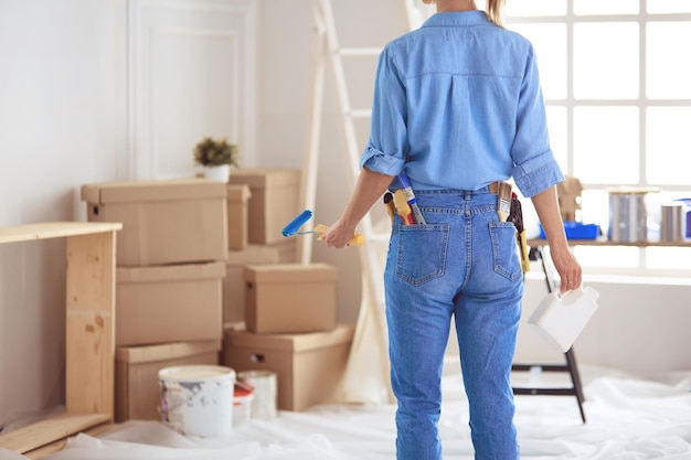 Mooie glimlachende vrouw die binnenmuur van huis schildert met verfroller