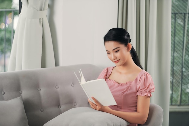 Mooie glimlachende vrouw die een boek leest en op de bank in de woonkamer ligt