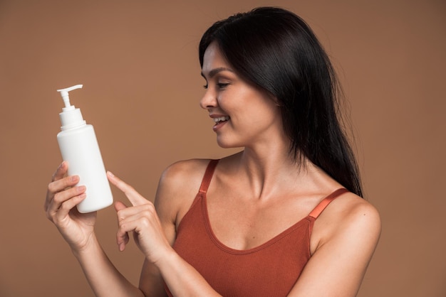 Foto mooie glimlachende vrouw houdt plastic pompfles met cosmetica vast in studio