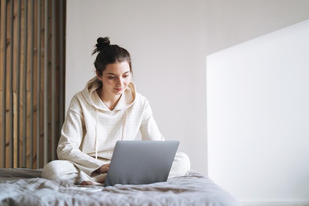 Mooie glimlachende vrouw met donker lang haar in casual met behulp van laptop op bed thuis