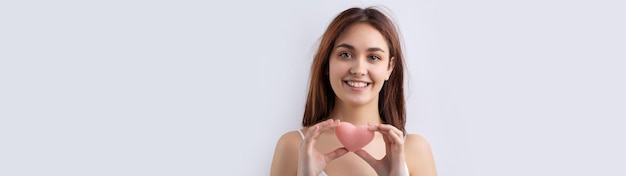 Mooie glimlachende vrouw met schone huid, natuurlijke make-up en witte tanden op een grijze achtergrond met een roze hygiënisch hart