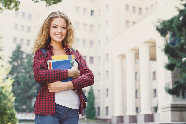 Mooie glimlachende vrouwelijke student die notebooks in handen houdt terwijl hij voor de universiteitscampus staat. Onderwijsconcept, kopieer ruimte