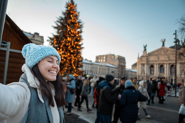 Mooie glimlachende vrouwen die een selfie-foto maken bij de vierkante kerstboom van de stad op de achtergrond