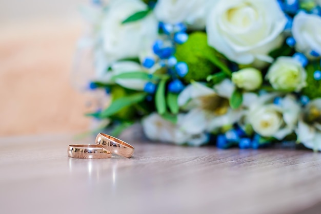 Foto mooie gouden trouwringen op tafel naast het bruidsboeket van witte en blauwe bloemen