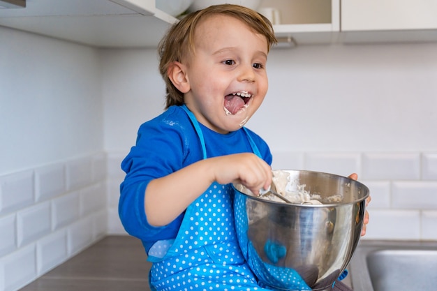 Mooie grappige blonde kleine peuter jongen bakken cake en muffins in binnenlandse keuken