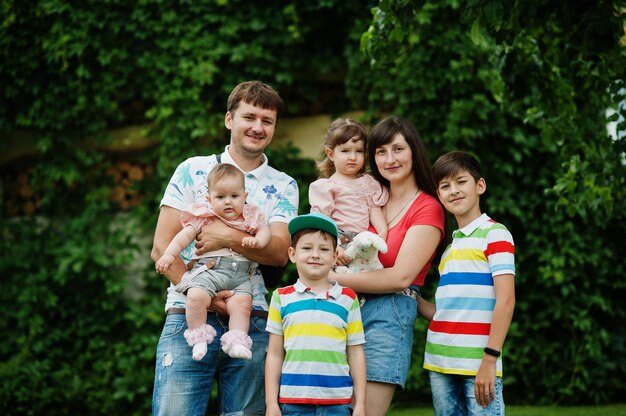 Mooie grote familie met jonge ouders en vier kinderen staan in groen gras op de binnenplaats.