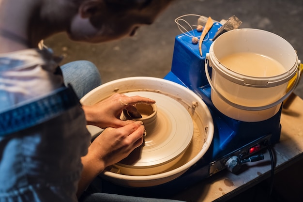 Mooie handen van een jong meisje, gekleurd met klei bij het modelleren van een pot op een pottenbakkersschijf in de werkplaats.