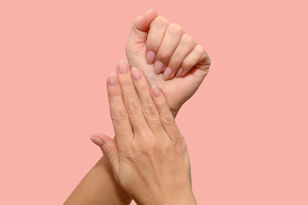 Mooie handen van een jonge vrouw. Natuurlijke manicure. Schone huid. Op een roze achtergrond.