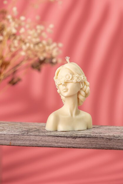 Mooie handgemaakte kaars in de vorm van een vrouwelijk lichaam op een houten standaard en roze achtergrond