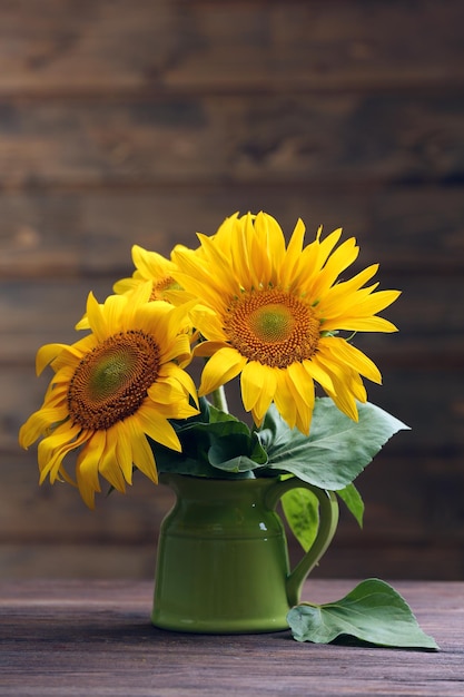Mooie heldere zonnebloemen in kruik op houten achtergrond