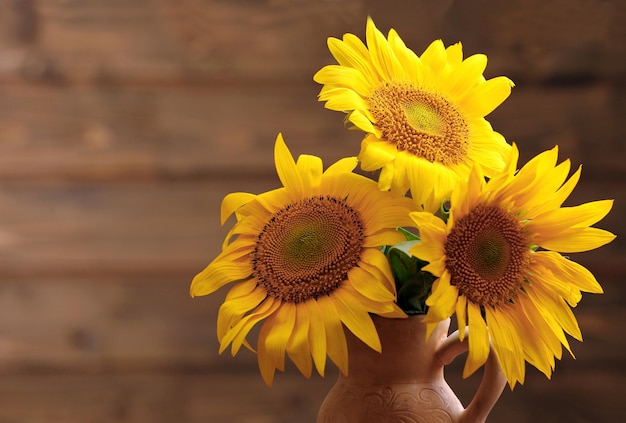 Mooie heldere zonnebloemen in kruik op houten achtergrond