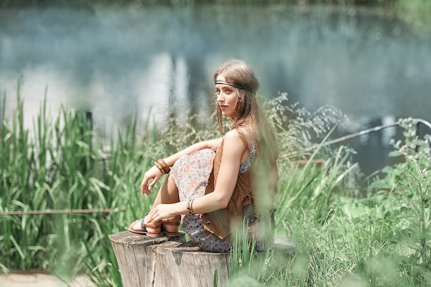 Mooie hippiemeisje, zittend op een boomstronk en kijken naar de vijver. het concept van eenheid met de natuur