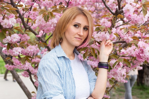 Mooie hipster vrouw in de buurt van sakura bloeiende boom Roze bloemen lente en jeugd concept Stijlvol meisje glimlachend Bloeiende tuin met kersenboom