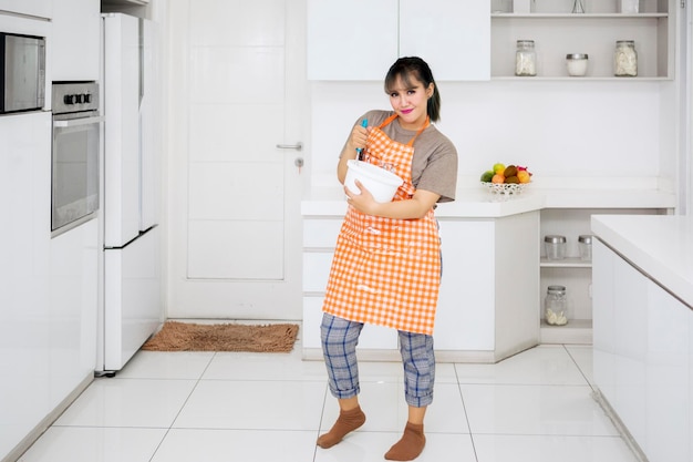 Mooie huisvrouw die deeg mengt in de keuken.