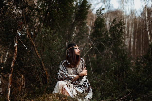 Mooie Indiaanse Amerikaanse vrouw met krijger sjamaan make-up zittend op de achtergrond van bossen