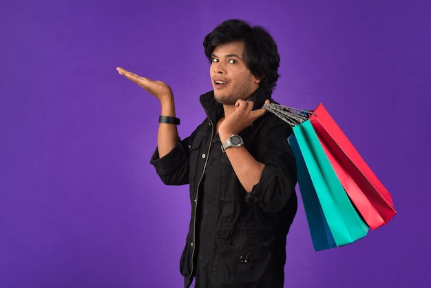 Mooie Indiase jonge knappe man vasthouden en poseren met boodschappentassen op een paarse achtergrond