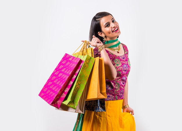 Mooie Indiase jonge meid die veel boodschappentassen vasthoudt terwijl ze traditionele etnische kleding draagt. Geïsoleerd op witte achtergrond