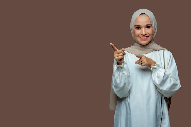 Mooie indonesische vrouw die hijab draagt, wijst glimlachend naar de linkerkant.