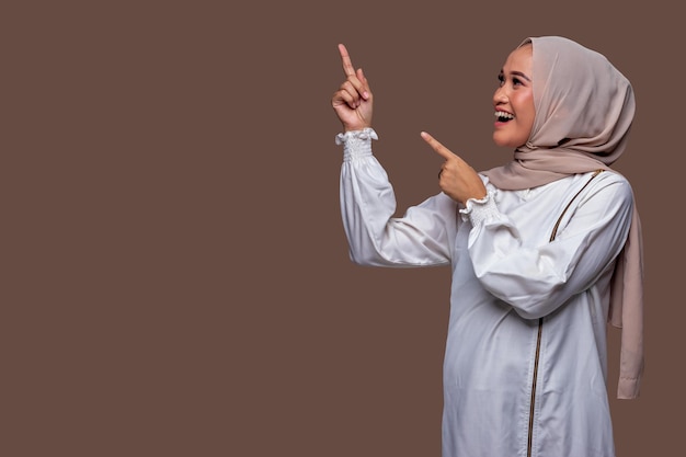 Mooie Indonesische vrouw in hijab wijst met een lachende uitdrukking naar linksboven.