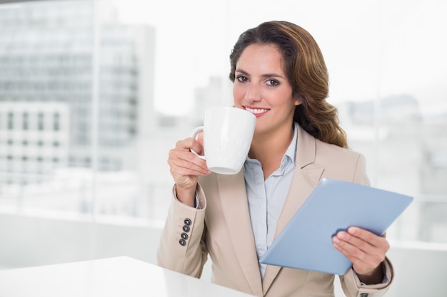 Mooie inhoudsonderneemster die tablet het drinken koffie gebruikt