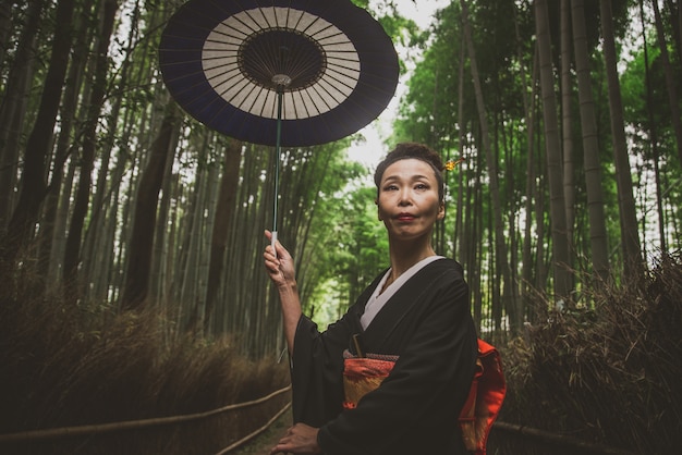 Mooie japanse hogere vrouw die in het bamboebos loopt