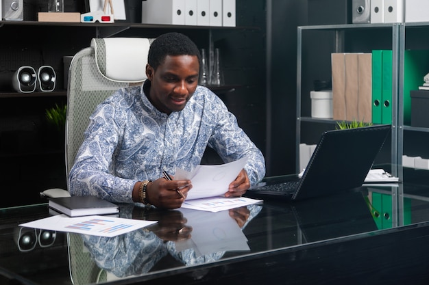 Mooie jonge Afrikaanse Amerikaanse zakenman die met documenten en laptop in bureau werkt