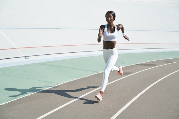 Mooie jonge Afrikaanse vrouw in sportkleding die buiten op het goede spoor loopt