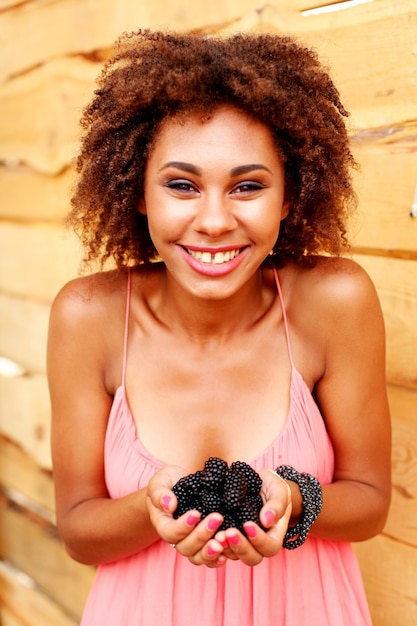 Mooie jonge Afrikaanse vrouw met afrohaar die verse bessen eet