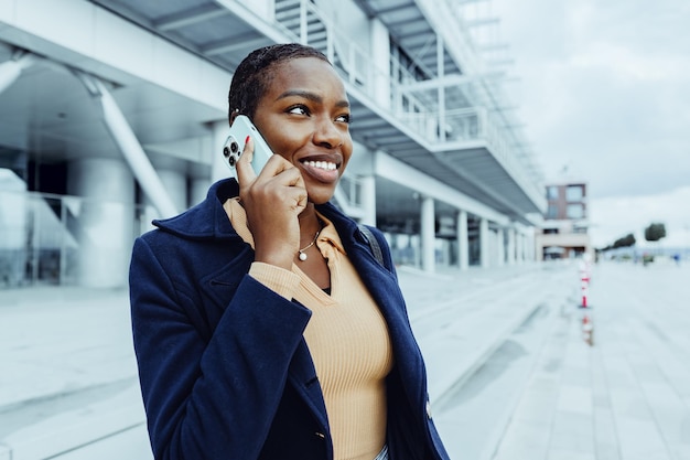 Mooie jonge Afrikaanse vrouw met een mobiele telefoon op straat.