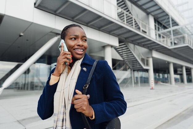 Mooie jonge Afrikaanse vrouw met een mobiele telefoon op straat.