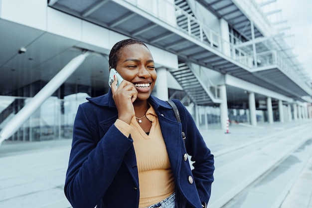 Mooie jonge Afrikaanse vrouw met een mobiele telefoon op straat.