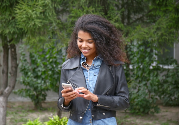 Mooie jonge Afro-Amerikaanse vrouw met mobiele telefoon buitenshuis