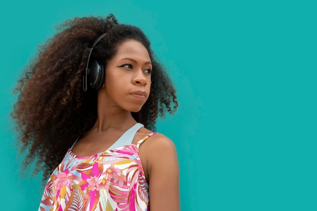 Mooie jonge afrovrouw in profiel met hoofdtelefoons op aquamarijnblauwe achtergrond
