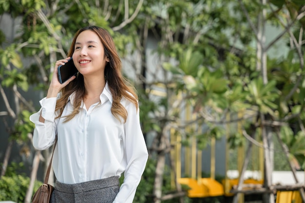 Mooie jonge Aziatische vrouw die belt en praat via de telefoon of mobiele telefoon in de stad