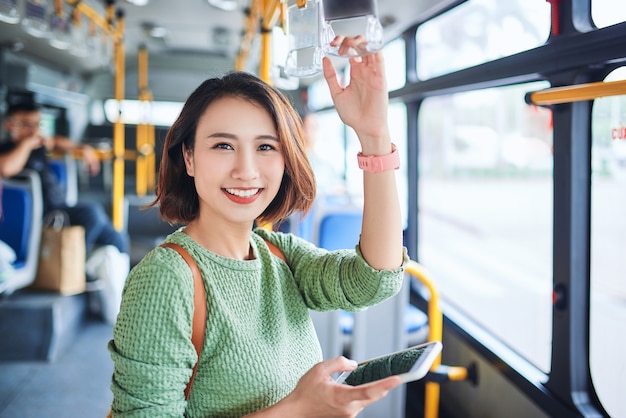 Mooie jonge aziatische vrouw die een smartphone in de stadsbus ziet